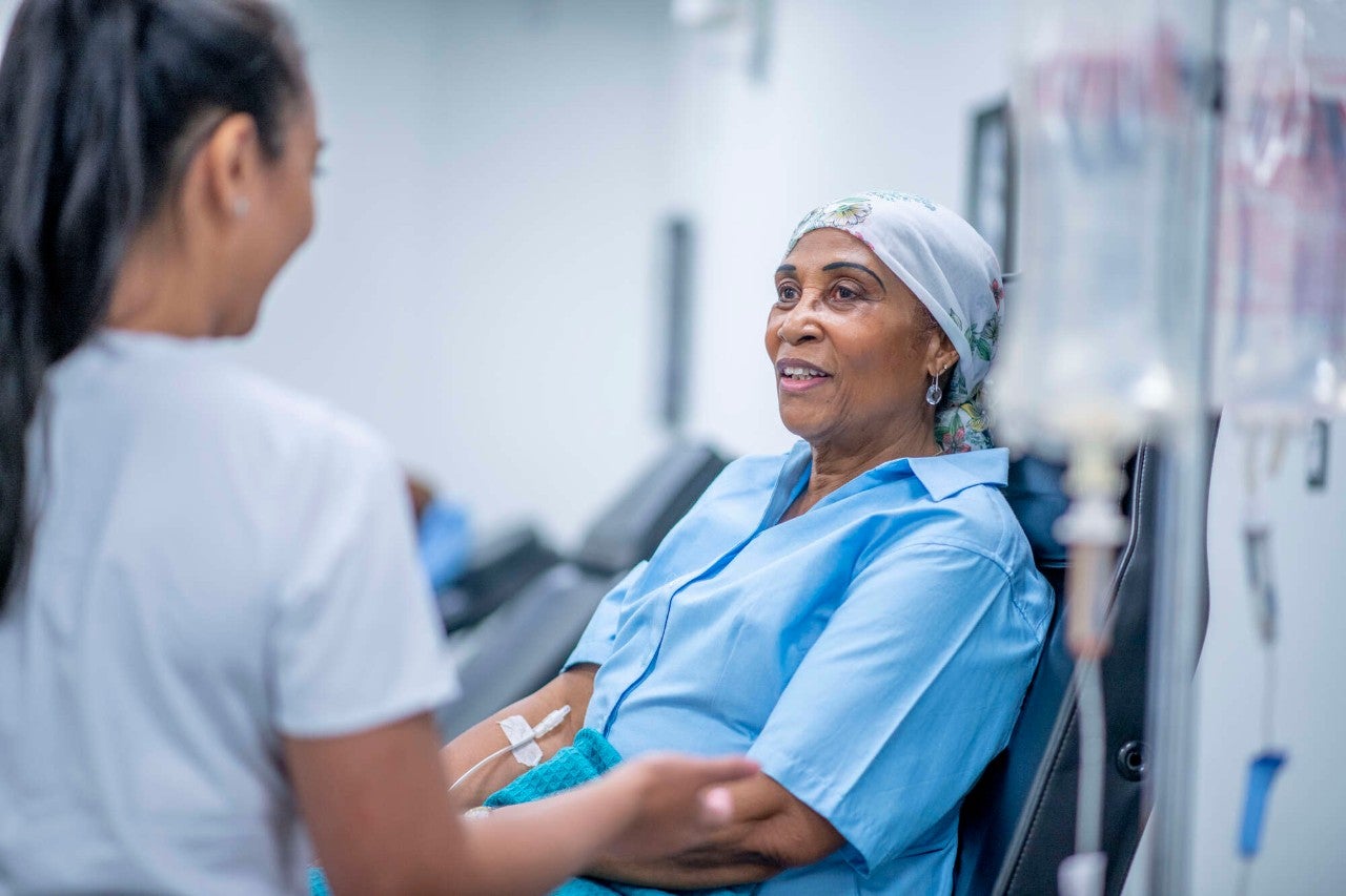A woman wearing a head scarf recovers from chemo treatment in the hospital. A doctor speaks with her and offers her support.