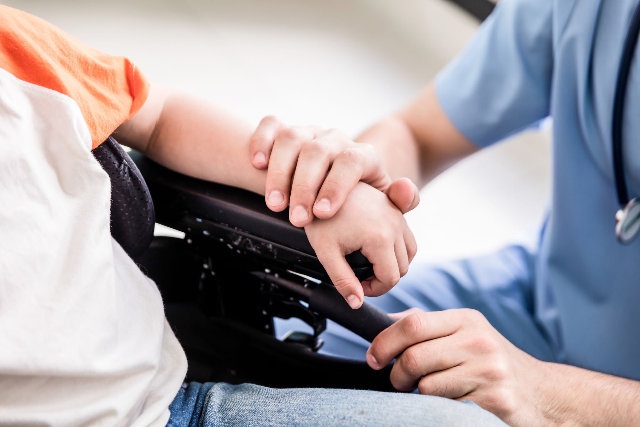 Close up of pediatrician putting his hand on patient on wheelchair