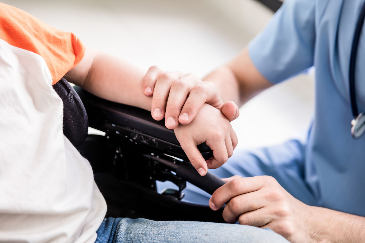 Close up of pediatrician putting his hand on patient on wheelchair